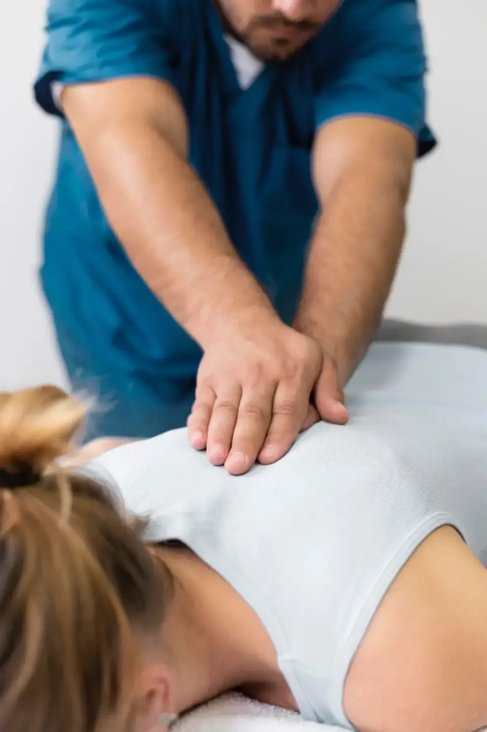 Physiotherapeut mobilisiert mit beiden Händen den Rücken einer Patientin