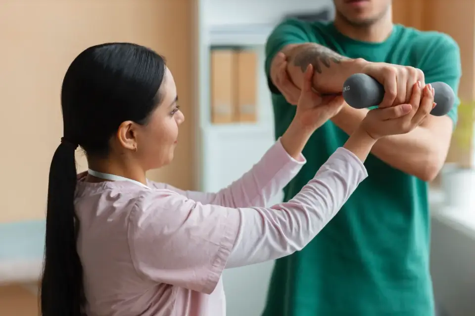 Therapeut unterstützt eine Patientin bei einer Armübung mit Gewicht