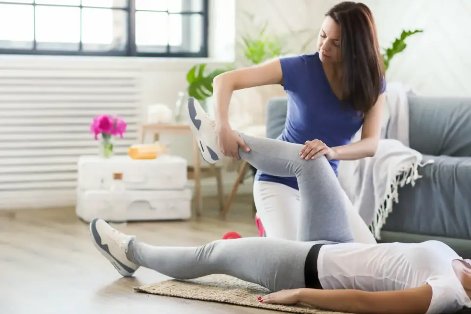Therapeutin mobilisiert das Knie einer liegenden Patientin